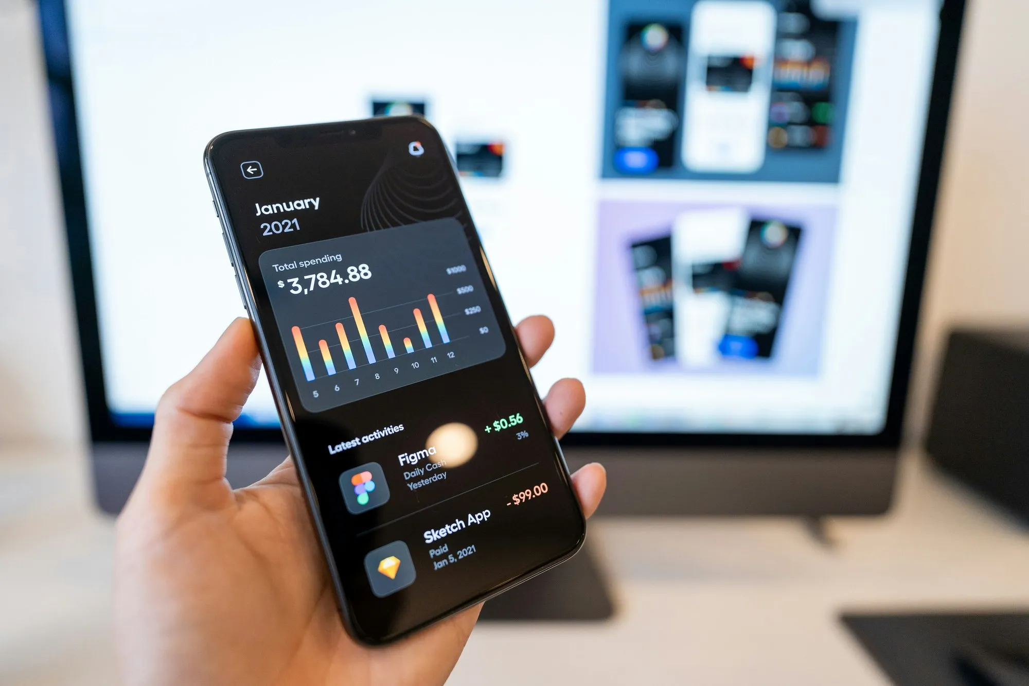A hand holding a phone with a dark spending overview and colourful bars