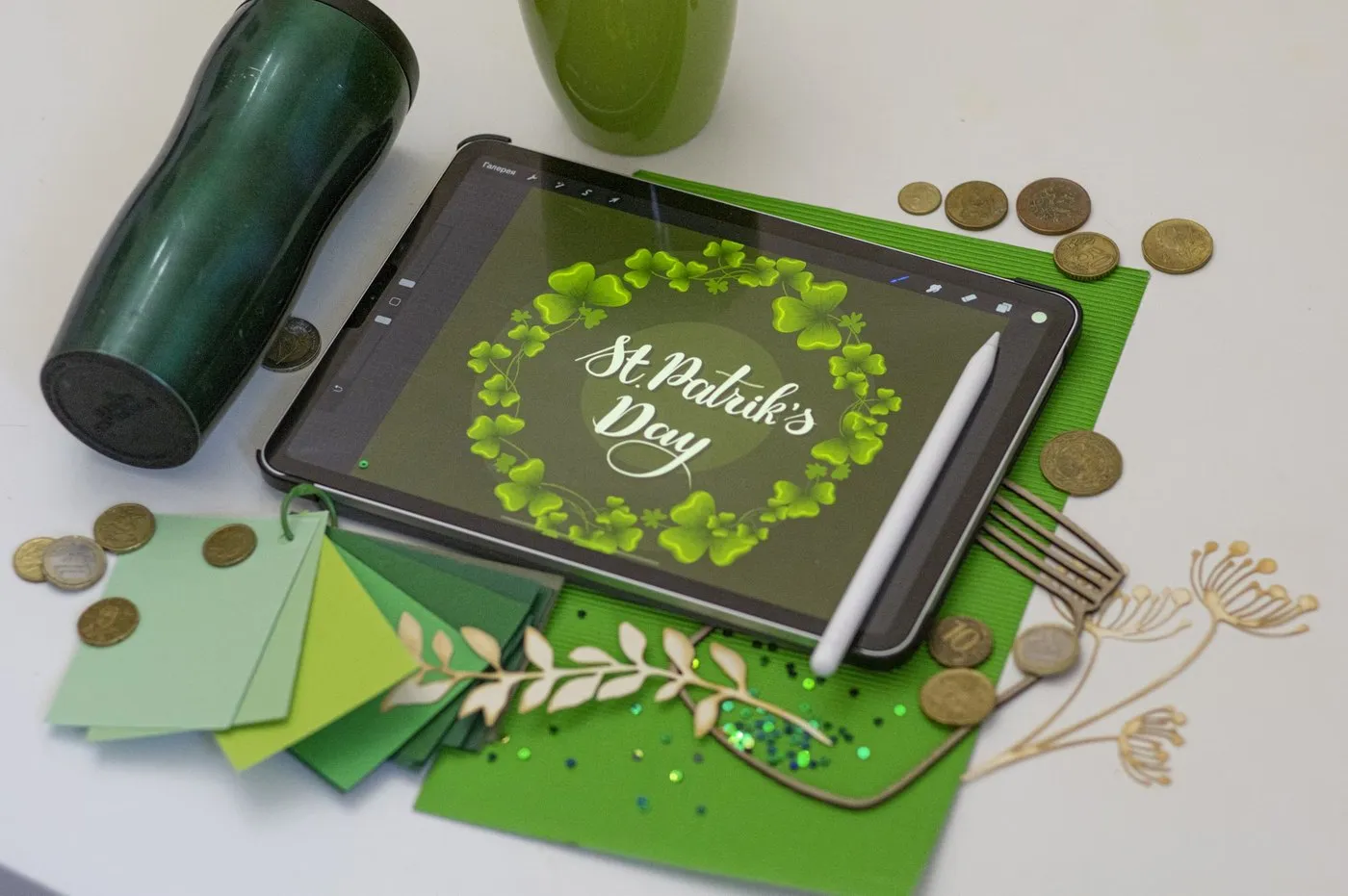 Tablet with hand-lettered “St Patrick’s Day” artwork, a stylus, coins and green paper on a desk