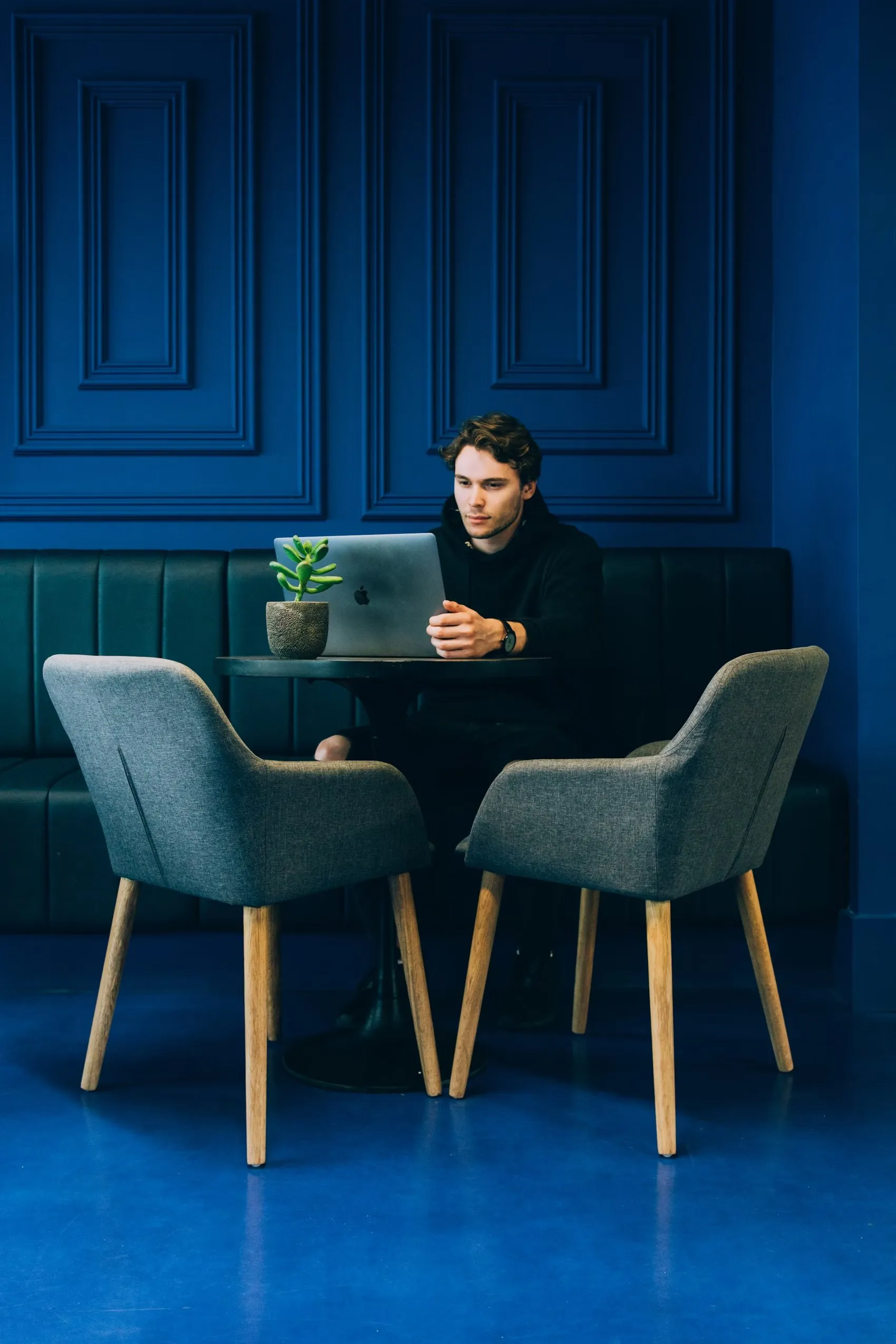 A designer working on a laptop at a café table in a deep blue room