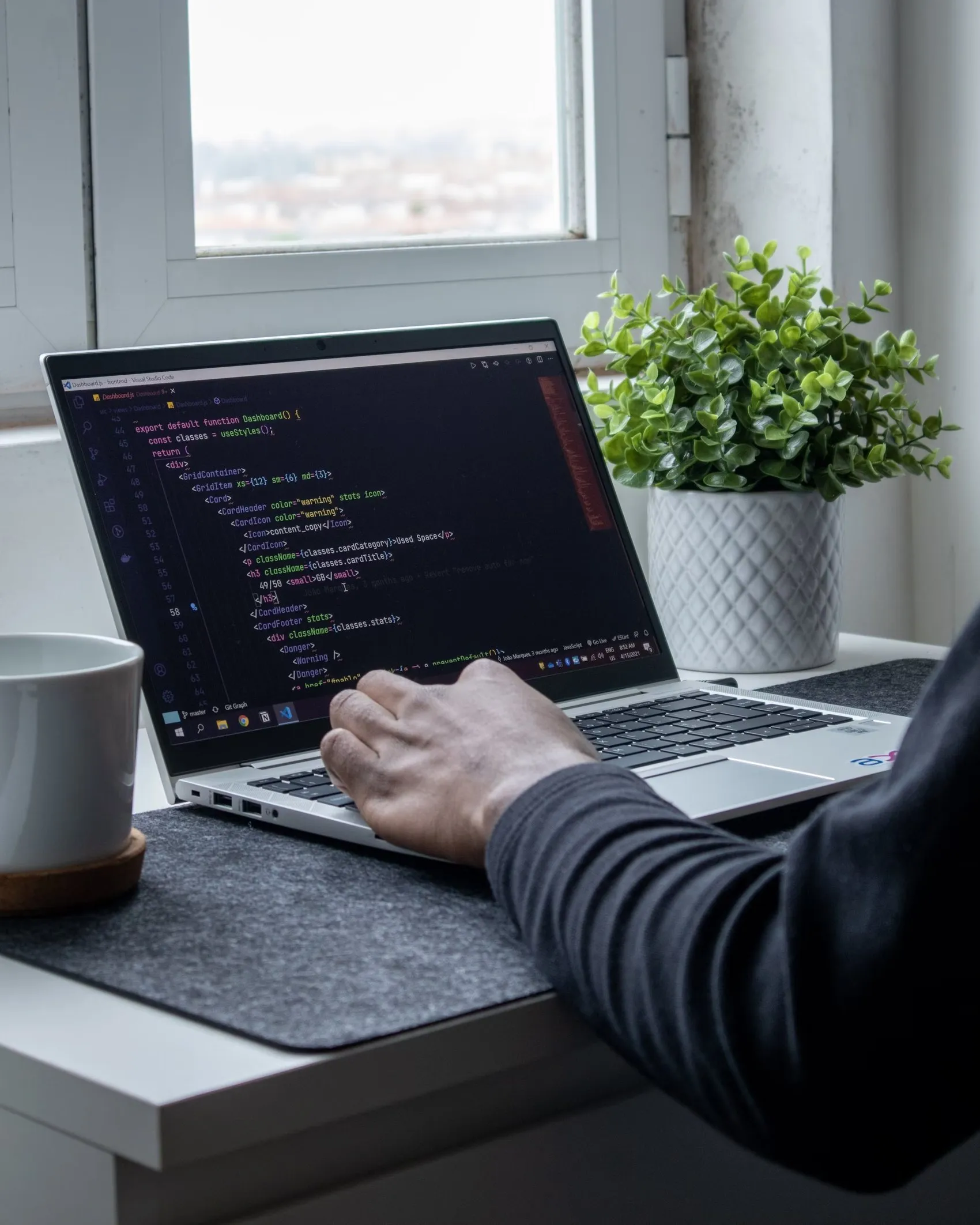 Laptop with code on screen next to a potted plant