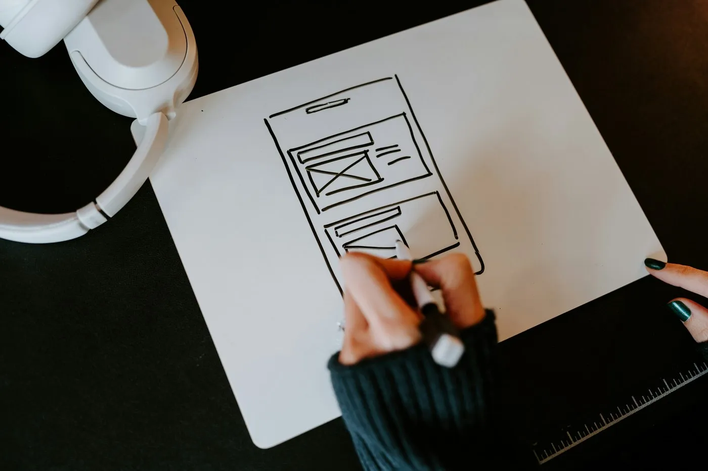 A hand sketching a mobile app wireframe on paper on a dark desk