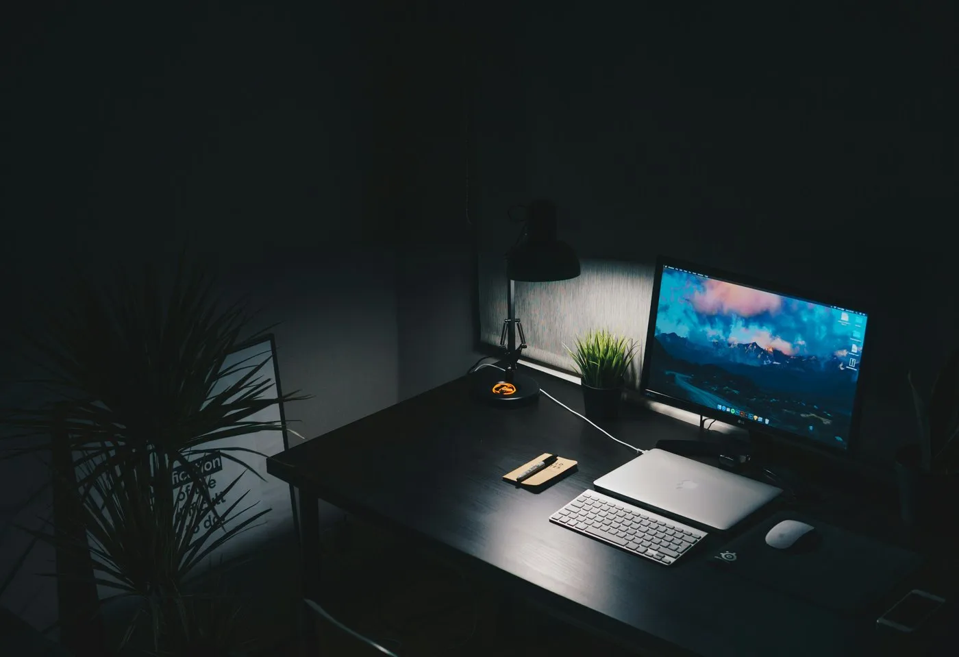 A designer’s desk with a monitor and laptop in a dark room lit by a desk lamp